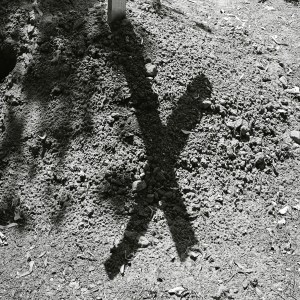 Der Schatten eines Holzkreuzes vom Grab eines unlängst Beerdigten auf einem Friedhof.