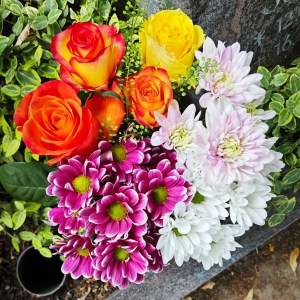 Ein bunter Blumenstrauß aus orangen, gelben, violetten und weißen Blüten als Blumenstrauß an einem Grabstein.