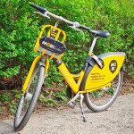 Ein gelbes Citybike steht vor einer grünen Hecke.